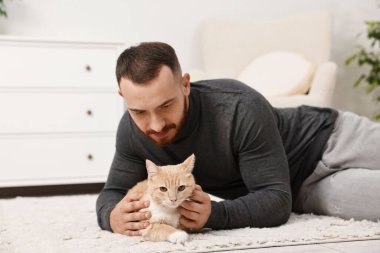 Evdeki sevimli kızıl kediyi okşayan adam.