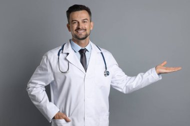 Steteskoplu gülümseyen doktor gri arka planda bir şeye bakıyor.