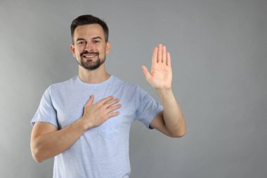 Adam gri arka planda el kaldırarak söz veriyor, mesaj için yer var. Yemin jesti