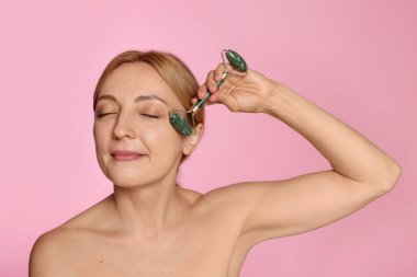 Güzel bir kadın pembe arka planda kendi kendine masaj yapıyor.