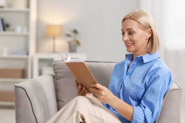 Gülümseyen orta yaşlı bir kadının portresi evde kitap okuyor.