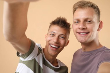 Mutlu kardeşler bej arka planda selfie çekiyorlar.