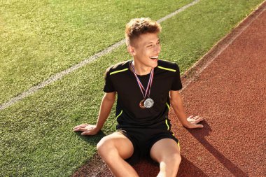 Mutlu kazanan farklı madalyalarla güneşli bir günde stadyumda oturuyor.