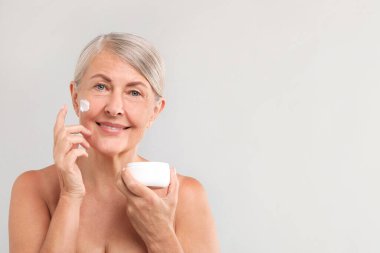 Işık arka planında yüz kremi olan son sınıf öğrencisi bir kadın. Metin için boşluk