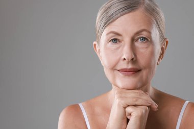Yüz masajı. Gri arka planda sağlıklı cilde sahip güzel bir kadın, mesaj için boşluk.
