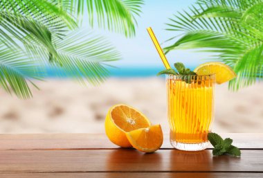 Plajdaki ahşap masada saman ve taze portakalla ferahlatıcı içecek.