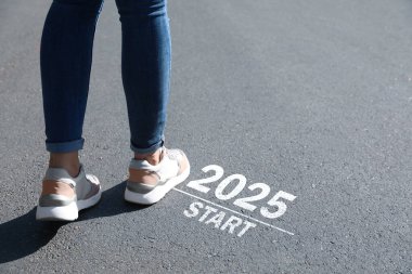 2025 işaretinin yanından geçen kadın asfaltta başlıyor, yakın plan. Yeni yıl kavramı, yeni bir başlangıç