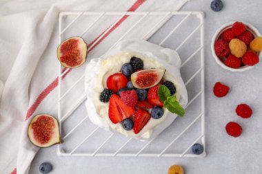 Krem şantili Pavlova pastası, taze böğürtlen, nane ve incir açık gri masada, düz konum