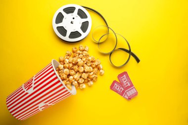 Film biletleri, patlamış mısır ve sarı arka planda film makarası.