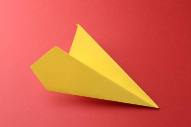 Kırmızı arkaplanda el yapımı sarı kağıt uçak.