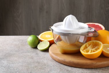 Plastic juicer and different citrus fruits on grey table. Space for text clipart