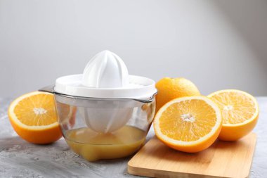 Plastik sıkacağı ve portakallar gri masada.