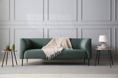 Rahat bir kanepe ve gri duvarın yanındaki yan masalar.