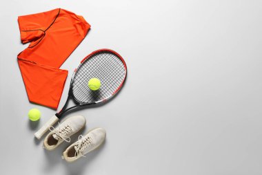 Tenis raketi, toplar, spor ayakkabılar ve gri arka planda turuncu gömlek, düz yatak. Metin için boşluk