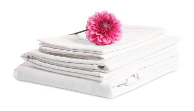 Stacked bed linens and pink flower on white background