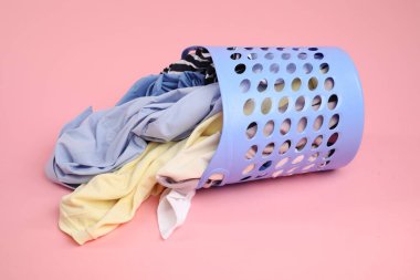 Pembe arka planda içi kıyafet dolu çamaşır sepeti devrilmiş.