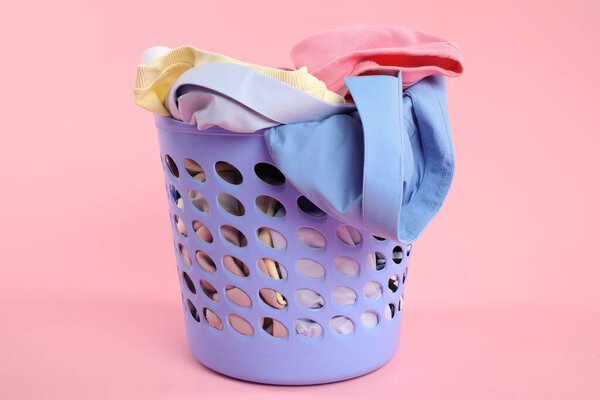 Пластиковая корзина, полная белья на розовом фоне