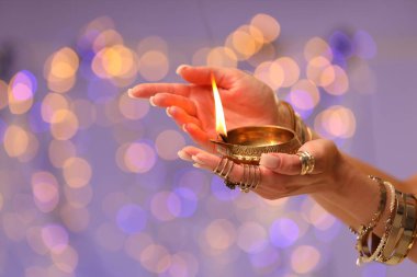 Diwali kutlaması. Renkli arka planda yanan diya lambasını tutan bulanık ışıklı kadın, yakın plan