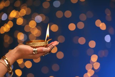 Diwali kutlaması. Mavi arka planda yanan, bulanık ışıkları olan bir kadın, yakın plan. Metin için boşluk