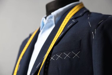 Semi-ready jacket, shirt and measuring tape on mannequin against gray background, closeup clipart