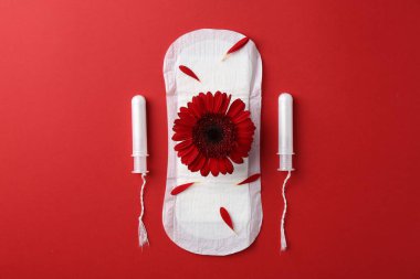 Kırmızı arka planda çiçekli ve tamponlu adet pedi.