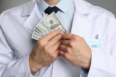 Yozlaşma konsepti. Doktor, gri arka planda ceketine dolar banknotları koyuyor.