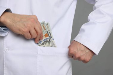 Yozlaşma konsepti. Doktor, gri arka planda cebine dolar banknotları koyuyor.