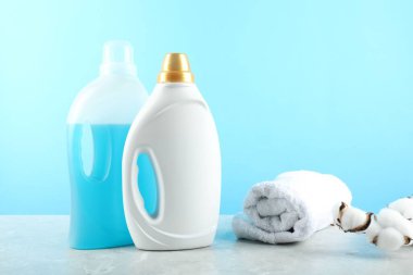 Şişelerde çamaşır deterjanı, havlu ve pamuk çiçekleri açık mavi arka planda gri mermer masa üzerinde