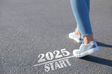 2025 işaretinin yanından geçen kadın asfaltta başlıyor, yakın plan. Yeni yıl kavramı, yeni bir başlangıç