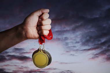 Altın, gümüş ve bronz madalyaları elinde tutan adam günbatımına karşı, yakın plan