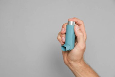 Gri arka planda astım spreyi tutan adam, yakın plan. Metin için boşluk