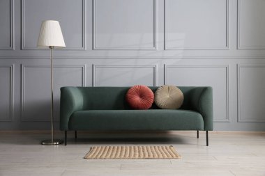 Gri duvarın yanında rahat bir kanepe ve lamba.