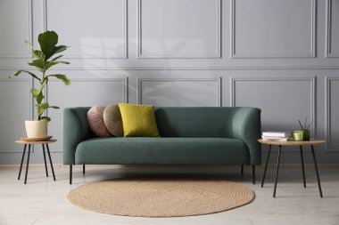 Rahat bir kanepe, ev bitkisi ve gri duvarın yanındaki masa.