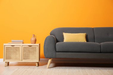 Yastıklı şık bir kanepe ve turuncu duvarın yanındaki sehpada kitaplar.