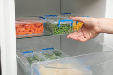 Buzdolabından donmuş yeşil bezelyeli plastik kap alan kadın, yakın plan.
