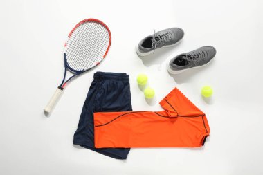 Tenis raketi, toplar, spor ayakkabıları ve arka planda spor giysileri.