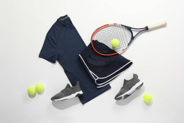 Tenis raketi, toplar, spor ayakkabıları ve arka planda spor giysileri.