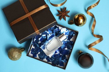 Hediye kutusunda parfüm şişesi ve açık mavi arka planda Noel dekoru, düz yatış.