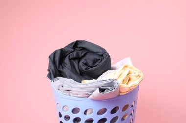 Pembe arka planda çamaşır dolu plastik sepet, yakın plan.