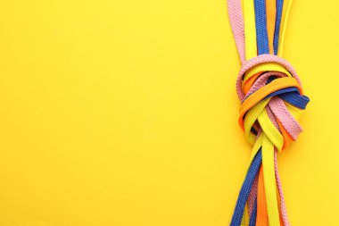 Sarı arkaplanda düğümlenmiş renkli ayakkabı bağcıkları, metin için yeri olan üst görünüm. Birlik kavramı