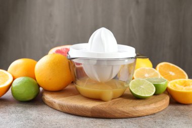 Plastik sıkacağı ve gri masada farklı turunçgil meyveleri.