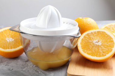 Plastik sıkacağı ve portakallar gri masada, yakın plan.