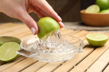 Woman squeezing juice of fresh lime with juicer at wooden table, closeup clipart