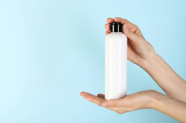 Açık mavi arka planda şampuan şişesi olan kadın, yakın plan. Metin için boşluk