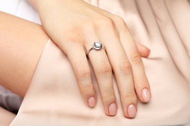 Bej kumaşa karşı değerli taşlı güzel bir yüzük takan kadın, yakın plan.