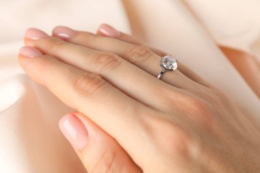 Bej kumaşa karşı değerli taşlı güzel bir yüzük takan kadın, yakın plan.