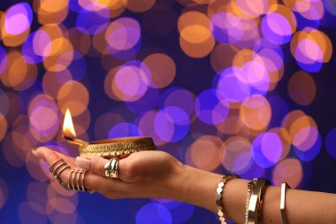 Diwali kutlaması. Renkli arka planda yanan diya lambasını tutan bulanık ışıklı kadın, yakın plan