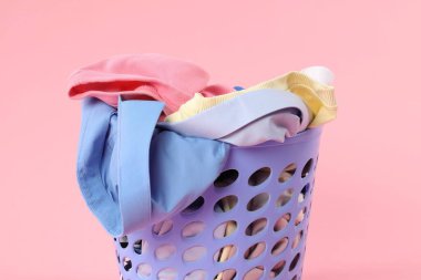 Pembe arka planda çamaşır dolu plastik sepet, yakın plan.