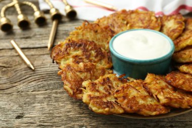 Lezzetli patates krepleri, ekşi krema, menorah ve ahşap masa üzerindeki mumlar, yakın plan. Hanuka bayramı yemekleri.