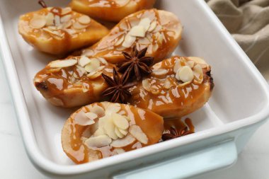 Delicious pears with caramel sauce, almond flakes and anise stars in baking dish on table, closeup clipart